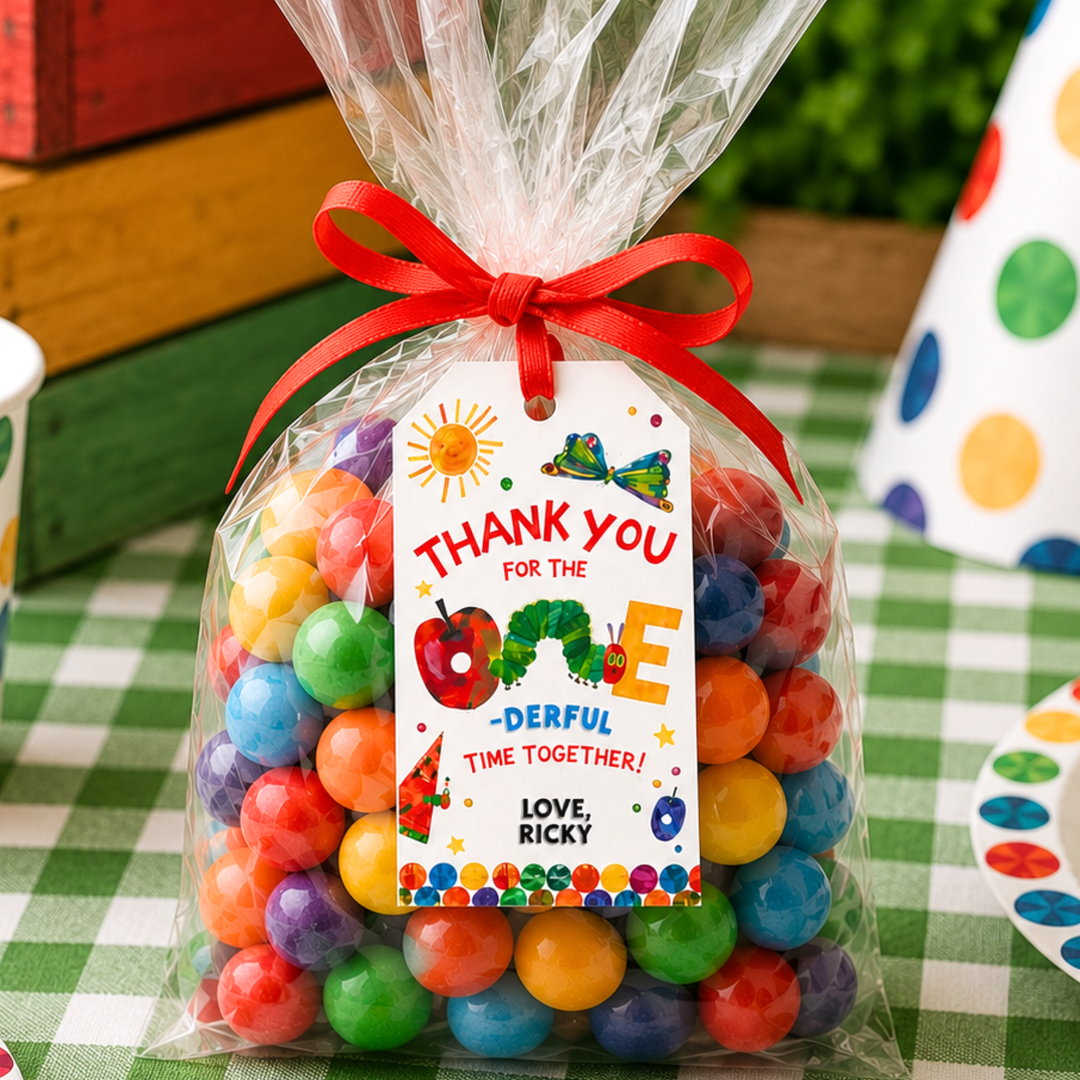 Very Hungry Caterpillar birthday gift tag printable tied to a clear candy favor bag filled with colorful gumballs, styled on a green checkered party table with wooden crates and festive birthday decorations for kids party favors.