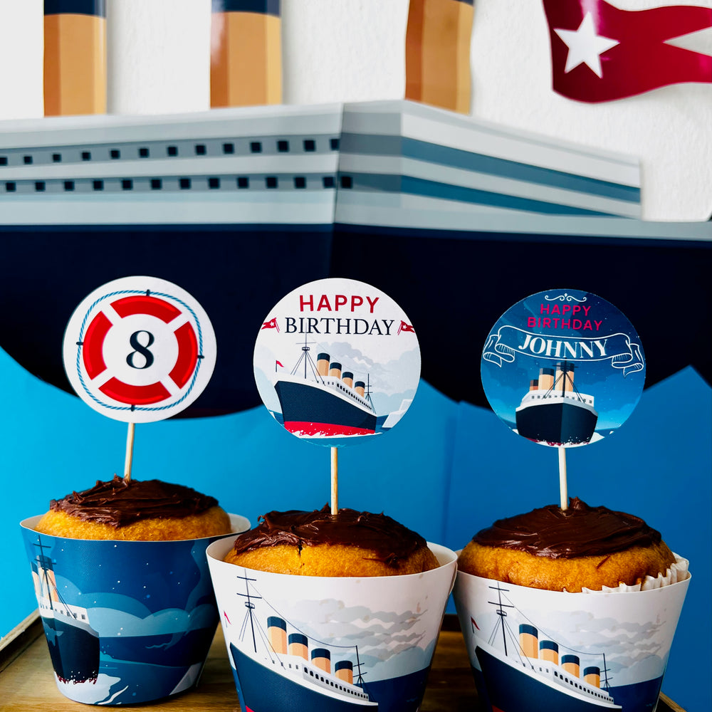 Cupcakes with nautical-themed wrappers and toppers in front of a ship model.