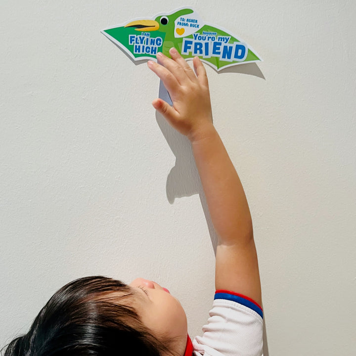Child holding up a green dinosaur valentines gift holder printable